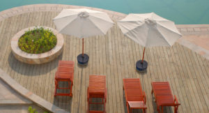 Two canopy umbrellas, each held up by a Gravipod, by a pool with four beach chairs and a planter.